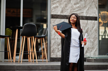 Young female african american student with diploma poses outdoors.