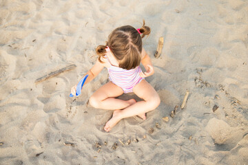 Caucasian child girl playing with sand and driftwoods while sitting on the beach, top view.