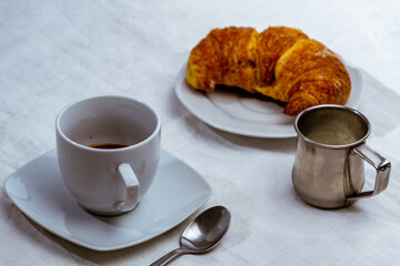 still life con taza de cafe con medialuna y jarra con leche sobre mantel blanco