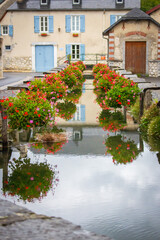 Fototapeta na wymiar Typical village street with canal and flowers in France. Ancient houses with flowers and medieval canal with reflection in water. Picturesque landmark of french village. Travel concept. 