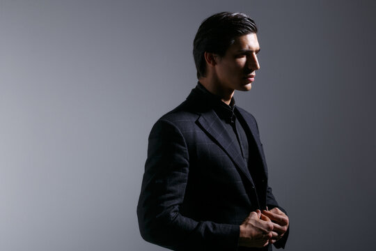 Profile portrait of handsome young man in black stylish suit, isolated on grey background. Horizontal view.