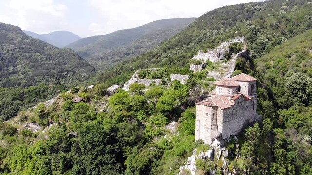 Medieval Fortress on a hill in eastern Europe, Bulgaria. Bulgarian antique and heritage stronghold fortification on a rock. Aerial video of a holy place and monastery. Tourist place with forest. Drone