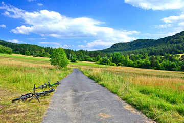 Fototapeta na wymiar Mountain biking in summer sunny day. Two bikes are lying on the ground, next to a asphalt dirt road. 