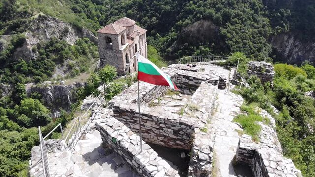 Medieval Fortress on a hill in eastern Europe, Bulgaria. Bulgarian antique and heritage stronghold fortification on a rock. Aerial video of a holy place and monastery. Tourist place with forest. Drone