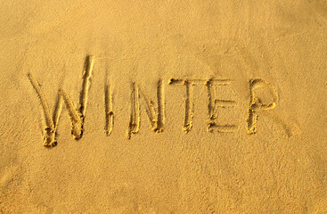 Winter word on beach sand. Winter printed on a yellow sand, top view. 