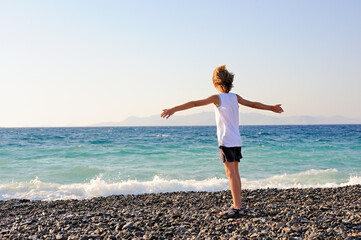 a boy on the seashore with his arms outstretched and the wind in his hair