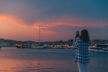 woman taking picture of the sunset over sea dock on her phone
