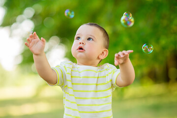 Happy baby boy one year plays with soap bubbles summer outdoors. Children's Lystyle