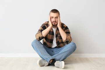 Depressed man sitting on floor near light wall