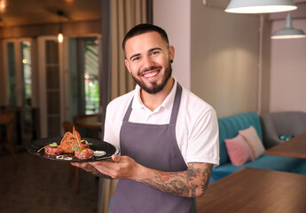 Young male waiter with dish in restaurant