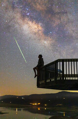 Main sitting on edge of railing looking at a meteor and the Milky Way over Lake Henshaw in California.