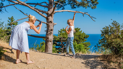 A woman takes pictures of her child on the sea against a tree
