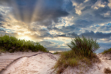 Wooden path through sand dunes on the Baltic sea in Ventspils against the backdrop of a dramatic sunrise or sunset