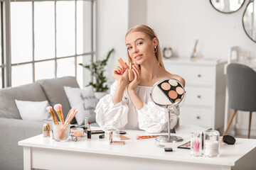 Beautiful young woman applying foundation at home