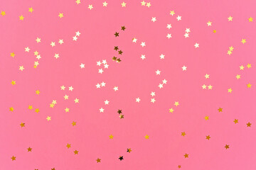 Photo of gold colored stars glitter sprinkles on pink trendy background. Festive holiday background for your projects. Celebration concept. Top view, flat lay.