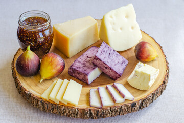 Figs, fig spread, vine soaked cheddar and assortment of various types of cheese on wooden cutting board