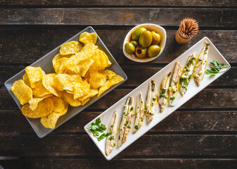 Three dishes with potato chips, picked anchovies and green olives on a dark wooden table with toothpicks. Typical Spanish snacks to eat in a bar. 
