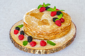 Delicious sweet crepes decorated with raspberries, blackberries and mint leaves on a beautiful wooden tray