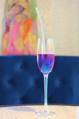 a glass with a straw and a drink of a purple hue on the background of a blue armchair