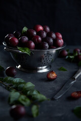 Juicy ripe plums lie in colander, on a dark background. The plum is cut with a knife.