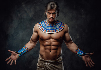 Athletic man in ancient egyptian costume posing in the studio with his hands wide opened