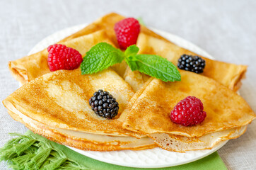 Delicious sweet crepes decorated with raspberries, blackberries and mint leaves close-up