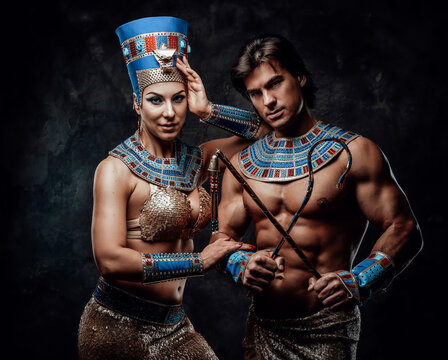 Woman in egyptian costume with her arm laid on male shoulder. Man holds the traditional egyptian signs of power. Both of them have blue and red bracelets.