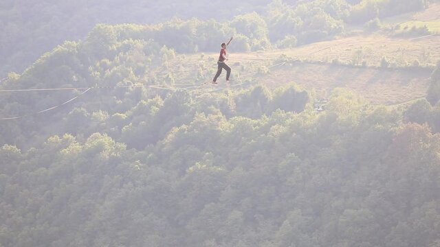 A man is walking along a stretched sling, Highline in the mountains, Man catches balance, Performance of a tightrope walker in nature, Highliner on the background of the mountains.