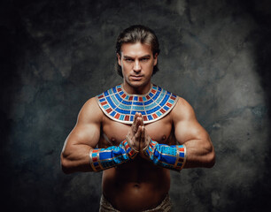 Athletic man in ancient egyptian costume posing in the studio with his palms in the sign of prayer