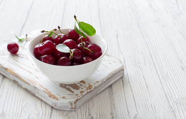 Ripe cherries in white bowl on white wooden background closeup