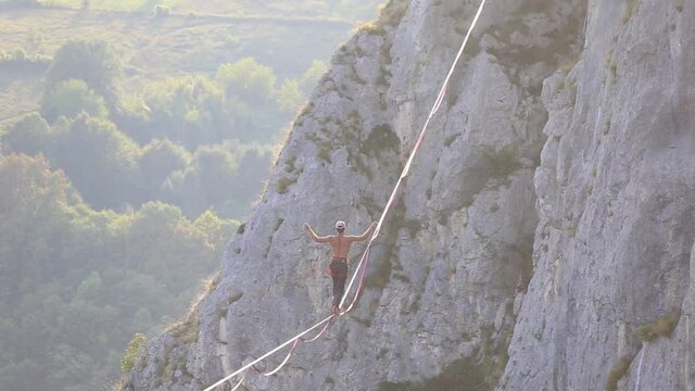 The man is trying to get up after a fall, A man on a stretched sling, Highline in the mountains, The man has lost balance, Performance of a tightrope walker, Highliner hanging on a rope, Fall athlete.