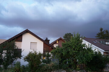 Fototapeta na wymiar Storm heavy clouds swelling above peaceful residential quarter on a summer evening in Urdorf, Switzerland.