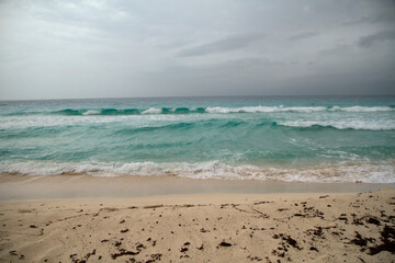 Vacations. Tropical seascape. Turquoise color water sea. The white sand and ocean waves under a dramatic stormy sky in Cancun, Mexico.