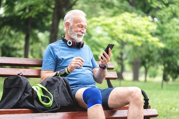 Senior man in sportswear using mobile phone fitness app sitting on park bench