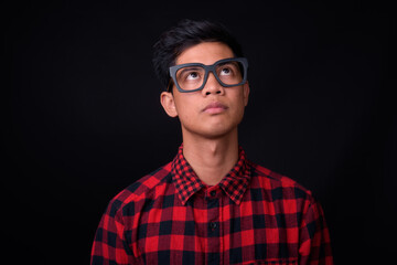Portrait of young Asian hipster man against black background