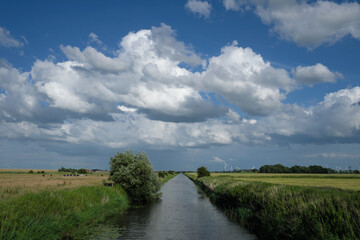 Ostfriesische Landschaft bei Dornumersiel in Niedersachsen mit Pumptief und starker Wolkenbildung mit blauem Himmel im Juni 2020 - Stockfoto