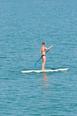 front view, very far distance, of a female, paddling a paddle board, in tropical water, on the gulf of Mexico, on a sunny morning