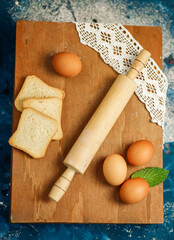 Set of rolling pin, flour, eggs, bread on a wooden background, top view.