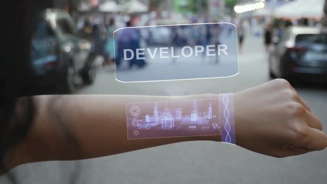 Female hand activates conceptual HUD holograms on smart bracelet with text Developer. Unrecognizable woman with holographic technology on a city street background