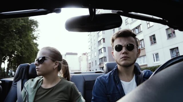 young couple in sunglasses ride in a convertible car around the city in summer.