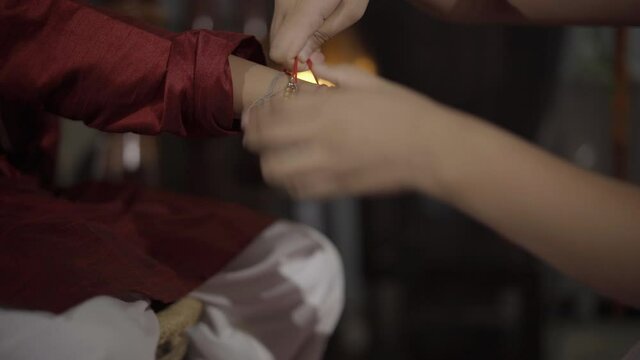Closeup of hands, sister tying rakhi, Raksha bandhan to brother's wrist during festival or ceremony - Raksha Bandhan celebrated across India as selfless love or relationship between brother and sister