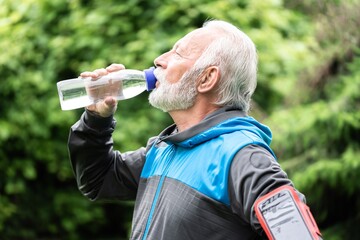 Senior sportsman drinking water while exercising outdoors