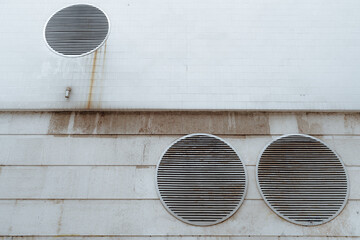 View of a dull futuristic wall in cyberpunk style with three huge round ventilation shafts covered with grills, rusty streaks on the tiled part above