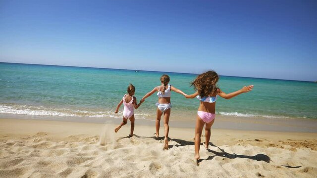 Authentic back view shot of happy healthy little girls are having fun and enjoying to run and splash a water in the sea on a sunny day during family holidays vacation.