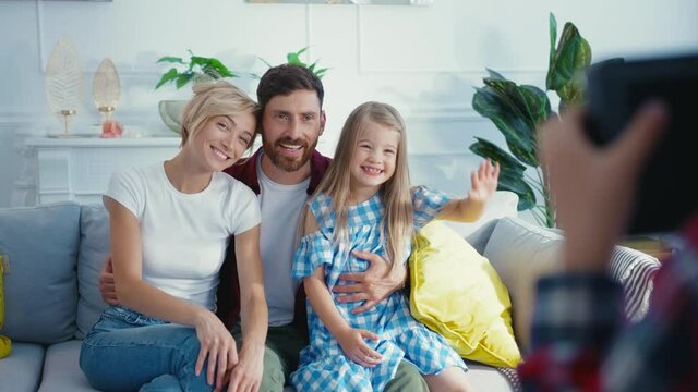 Little son taking family photographs on camera while his happy smiling parents and sister sitting on couch posing together. Photoshoot. Home entertainment.