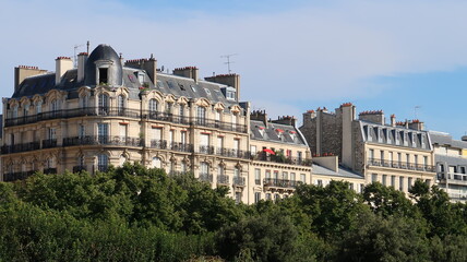 Fototapeta na wymiar Immobilier à Paris, vue sur des immeubles parisiens haussmanniens, émergeant au-dessus des arbres en été (France)