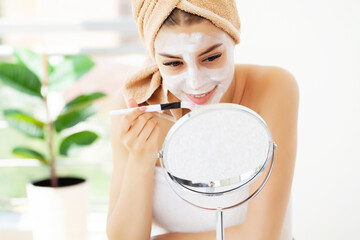 Woman applies white clay mask for facial skin care in hotel luxury bathroom