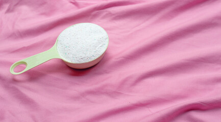 Obraz na płótnie Canvas Detergent powder in measuring spoon on pink cloth. Laundry concept.