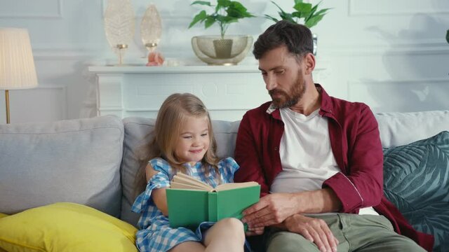 Happy caucasian father teaching his cute daughter reading a book remembering words doing homework enjoying. Distant education. Home entertainment. Leisure.