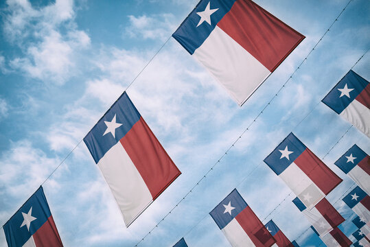 A group of Texas flags hanging against blue sky and white clouds